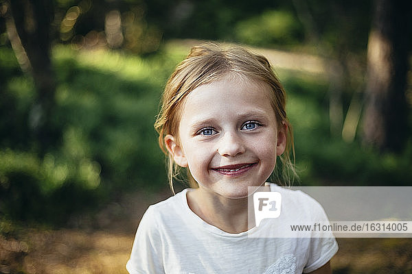 Portrait of cute smiling girl standing in forest