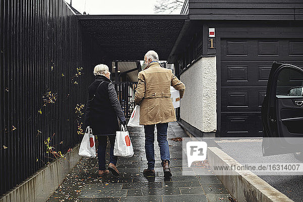 Rear view of senior couple with bags walking together on sidewalk during winter