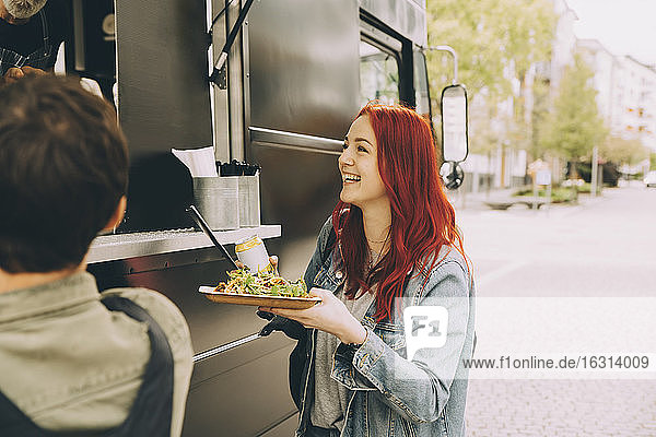 Lächelnde Kundin  die mit dem Besitzer spricht  während sie mit einem Speiseteller auf der Straße steht