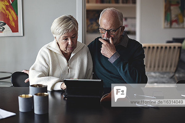 Älteres Ehepaar benutzt digitales Tablett  während es am Esstisch im Wohnzimmer sitzt