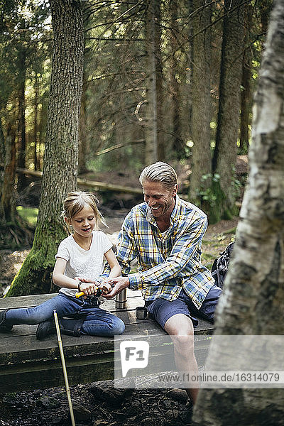 Lächelnder Vater hilft Tochter beim Einschlag auf Steg im Wald