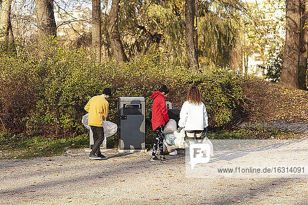 Junge männliche und weibliche Umweltschützer halten Abfälle an der Mülltonne