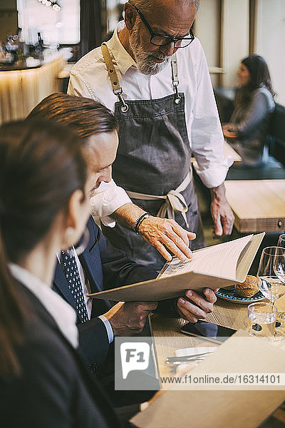 Waiter standing by table while business professionals sitting in restaurant