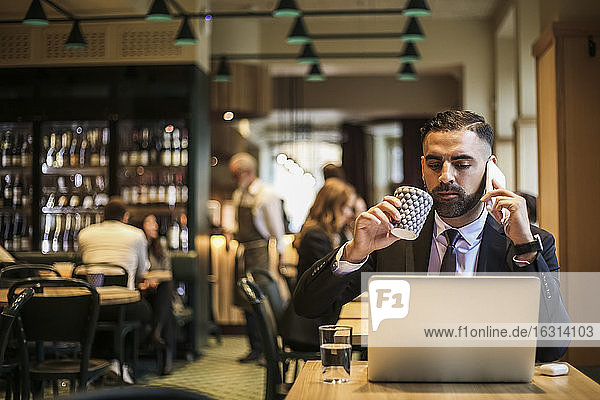 Businessman talking on phone while drinking coffee in restaurant