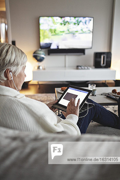 Ältere Frau benutzt digitales Tablet  während sie auf dem Sofa im Wohnzimmer sitzt