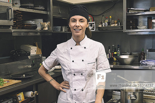 Portrait of smiling female chef with hand on hip in commercial kitchen