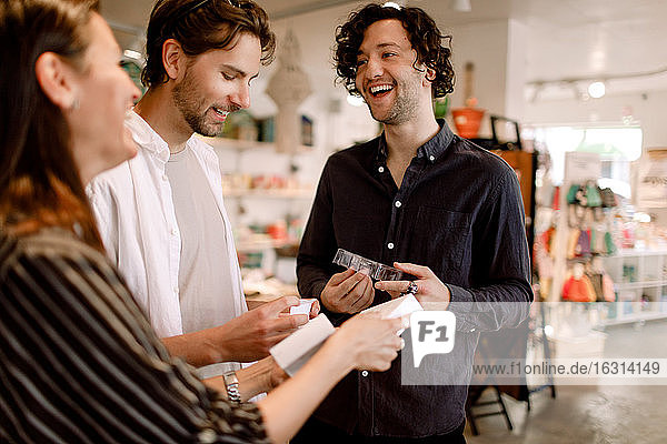 Smiling male friends talking to saleswoman in store