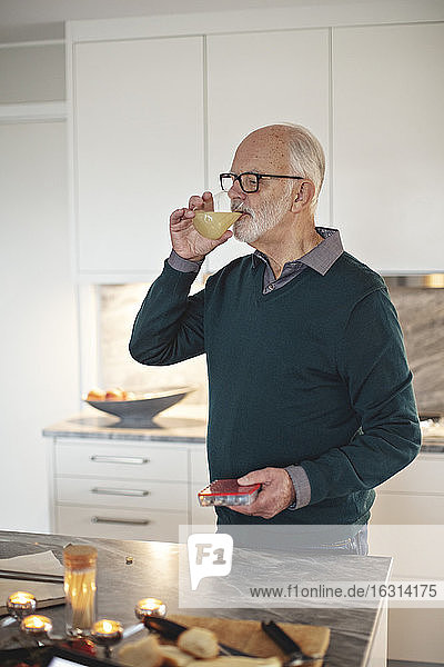 Älterer Mann trinkt Saft  während er zu Hause an der Kücheninsel steht