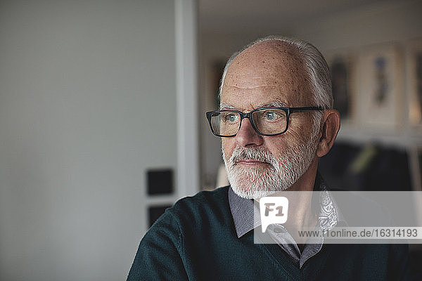 Kontemplierender älterer Mann  der eine Brille trägt  während er von zu Hause weg schaut