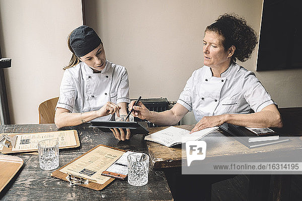 Female chefs discussing while sitting at table in restaurant