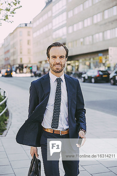 Porträt eines Geschäftsmannes mit Tasche und Telefon beim Spaziergang in der Stadt