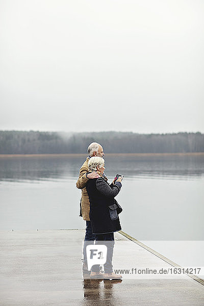 Full length of senior couple standing by lake against clear sky