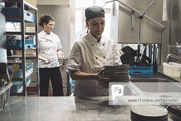 Female chef holding plates while coworker standing in background in commercial kitchen