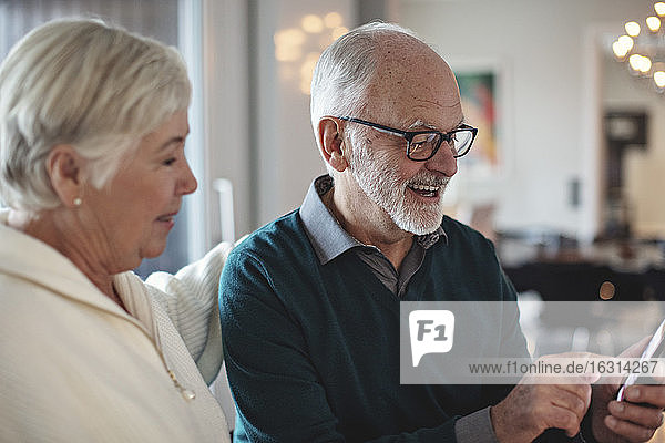Lächelndes älteres Paar  das im Wohnzimmer sitzt und ein Smartphone benutzt