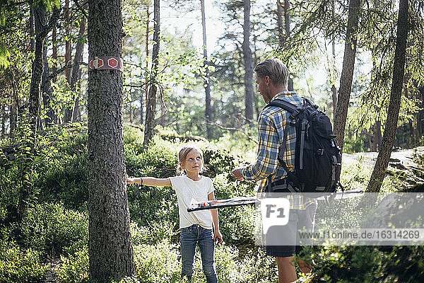 Tochter spricht mit Vater  während sie im Wald am Baumstamm steht