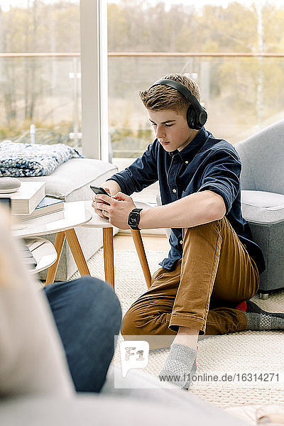 Teenager benutzt Mobiltelefon  während er zu Hause auf dem Boden sitzt