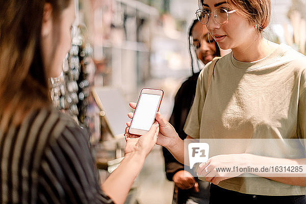 Frau zeigt Telefon einer Verkäuferin im Modegeschäft