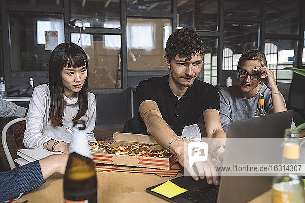 Lächelnde Kollegen mit Pizza am Arbeitsplatz