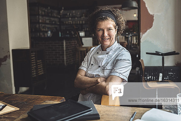 Porträt eines lächelnden reifen Kochs mit verschränkten Armen im Restaurant