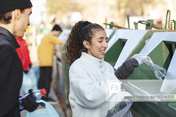 Lächelnde Umweltschützerin mit Freundin  die Abfall in den Mülleimer wirft