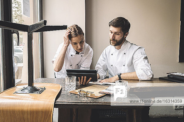 Chef with coworker looking at digital tablet at table in restaurant