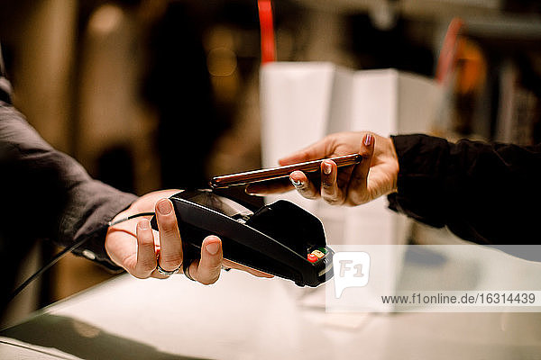 Cropped hand of female customer paying through phone at store