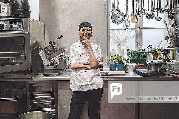 Porträt eines glücklichen reifen Kochs mit Hand am Kinn in der Großküche