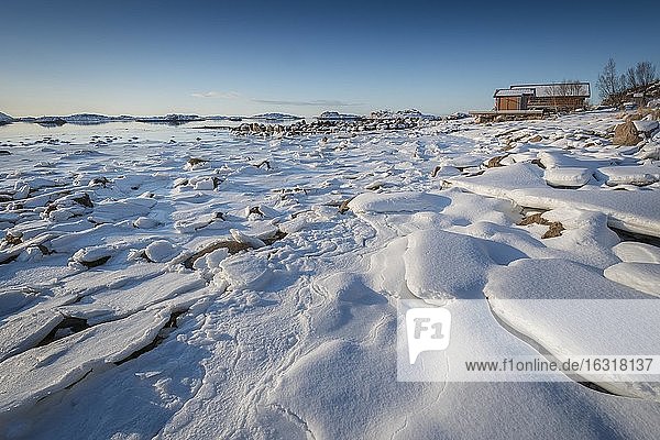 Holzhaus am Strand  gefrorener Fjord mit Eisschollen in Winterlandschaft  Nordland  Lofoten  Norwegen  Europa