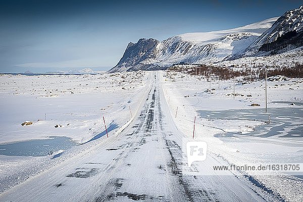 Iced snow road  in winter landscape  behind mountain range and sea  Nordland  Lofoten  Norway  Europe