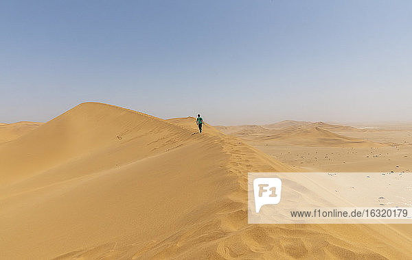 Boy walking along sunny desert sand dune ridge  Namibia
