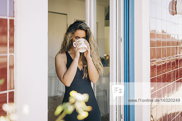 Porträt einer jungen Frau beim Kaffeetrinken in einer Verandatür