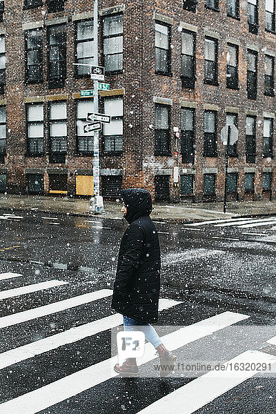 Junge Frau in warmer Jacke beim Überqueren einer verschneiten städtischen Straße  New York City  New York  USA