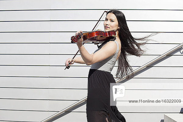 Porträt einer jungen Asiatin  die auf einer Treppe Geige spielt