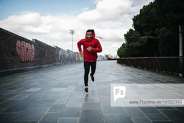 Lächelnder junger Mann mit rotem Kapuzenpulli beim Laufen in der Stadt