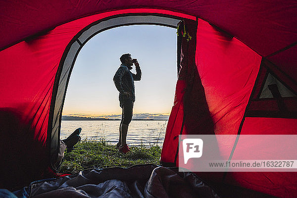 Mann zeltet in Estland  steht vor seinem Zelt und beobachtet den Sonnenuntergang