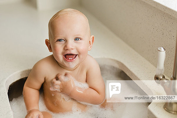 Portrait of laughing baby boy having fun while bathing in sink