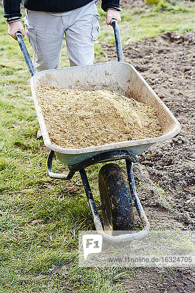 Mann transportiert Sand in einer Schubkarre