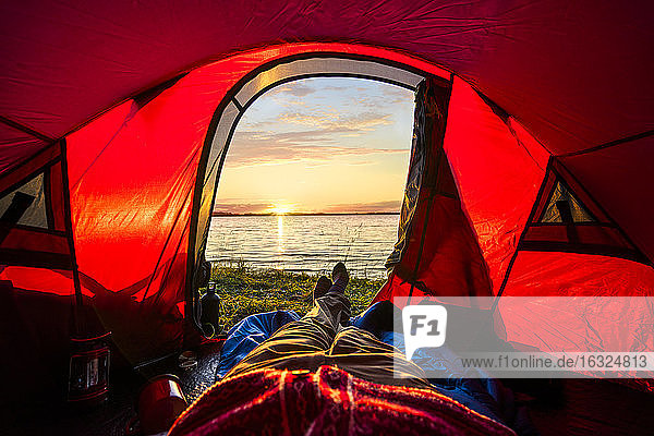 Man camping in Estonia, watching sunset lying in tent