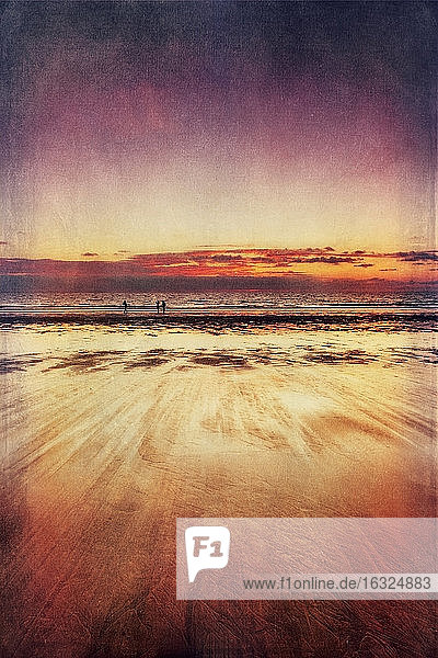 Drei Spaziergänger am Strand bei Sonnenuntergang