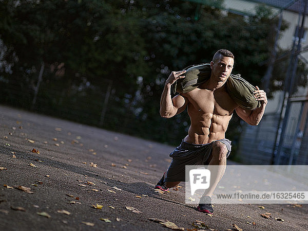 Muskulöser junger Mann trainiert mit Sandsack auf Sportplatz