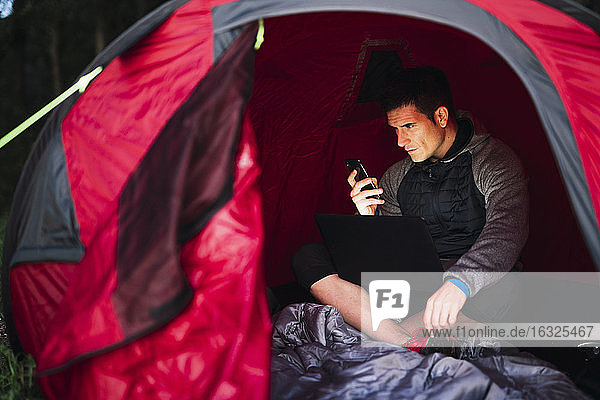 Mann zeltet in Estland  sitzt in seinem Zelt und benutzt sein Smartphone