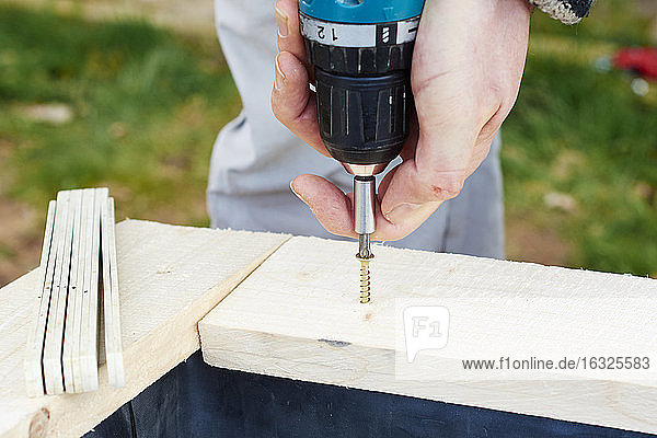 Gärtner schraubt Holzbohlen an  um ein Hochbeet zu bauen