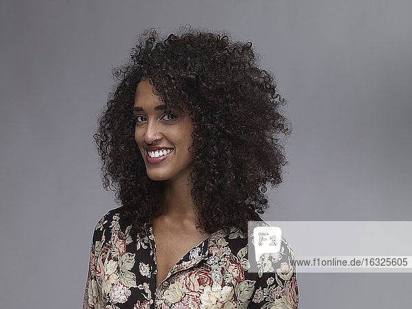 Portrait of smiling young woman with nose ring and Afro in front of grey background