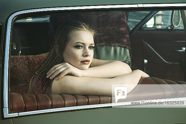 Portrait of young woman looking through rear window of vintage car