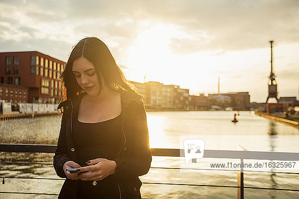 Deutschland  Münster  junge Frau schaut vor dem Stadthafen auf ihr Smartphone
