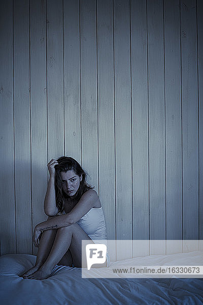 Sad young woman sitting on bed