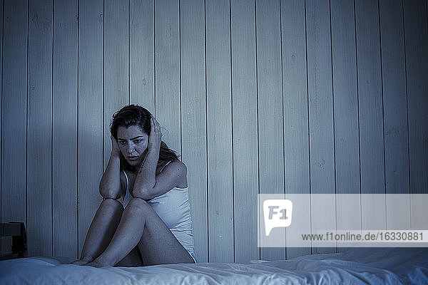 Sad young woman sitting on bed
