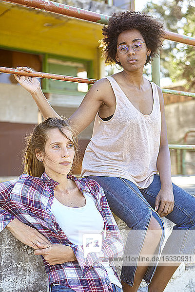 Young women looking away while sitting on wall