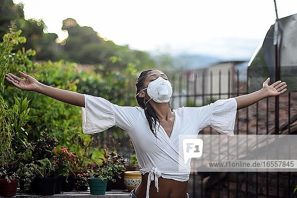 Junge schwarze Frau mit Gesichtsmaske öffnet ihre Arme und entspannt sich auf dem Balkon