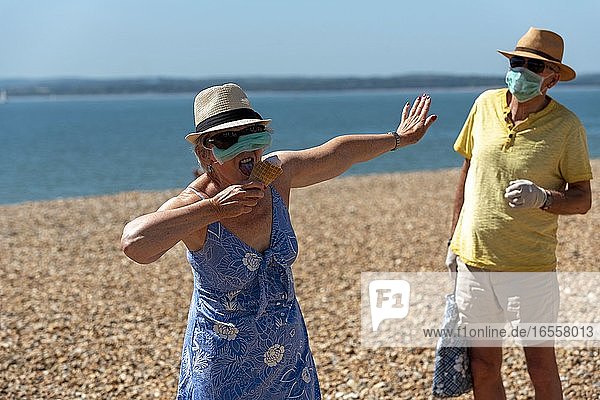 Southsea  Portsmouth  Southern England  UK. May 2020. Woman eating ice cream whilst wearing a mask and rubber protective gloves and social distancing from her husband during the Corvid-19 outbreak. On the beach in Southsea.